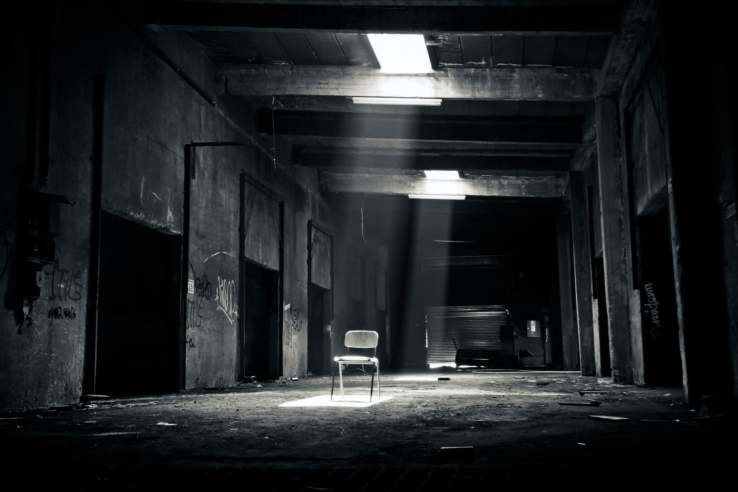 black and grey image of a folding chair in the middle of a dark warehouse space